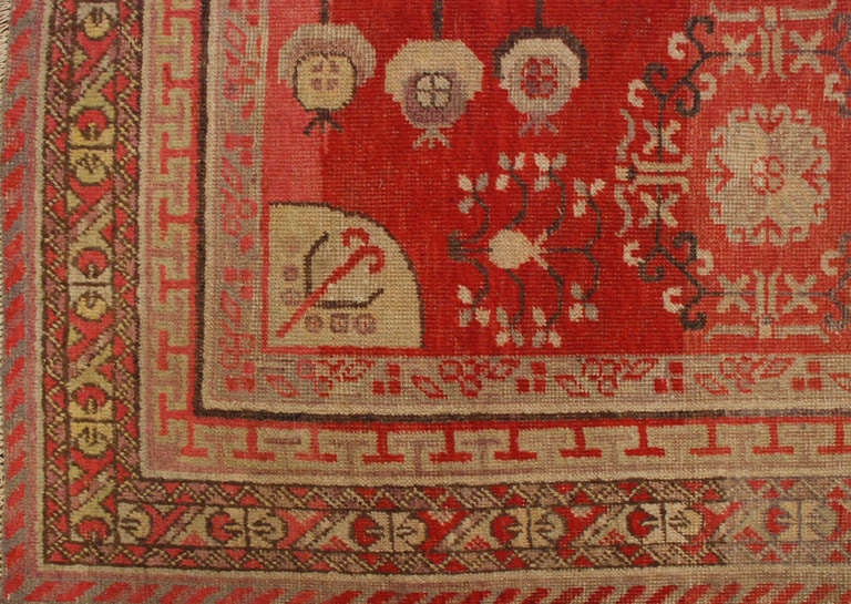 An early 20th century Central Asian Khotan rug with an unusual floral and geometric pattern in a crimson background surrounded by multiple complementary borders.

Measures: 4'5