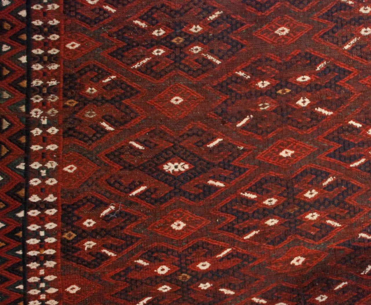 Tapis Sumak d'Asie centrale du début du XXe siècle, originaire du Turkménistan, présentant un motif géométrique sur un fond cramoisi, entouré de multiples bordures géométriques complémentaires.