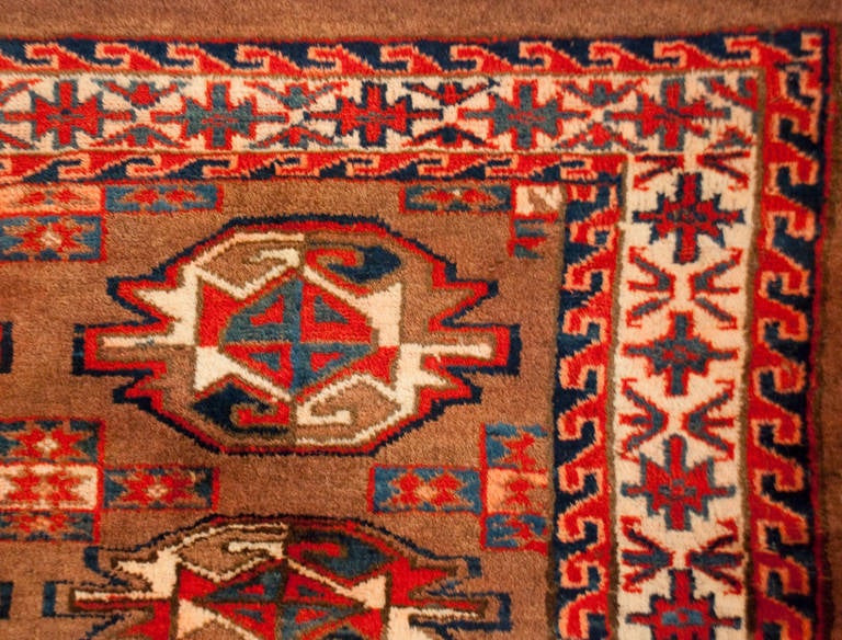 An early 20th century Persian Yamut with beautiful indigo, crimson, and natural wool colored geometric medallions on a natural brown background, surrounded by a complementary geometric border.