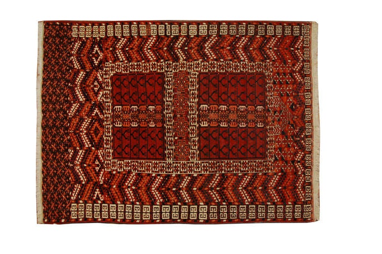 Alfombra de oración turcomana persa de principios del siglo XX con motivos geométricos tejidos en lana carmesí, naranja y marfil natural.