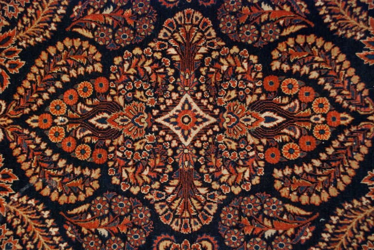 An early 20th century Persian Kashan rug with densely woven floral and leaf pattern on an indigo background, surrounded by a complementary floral border.