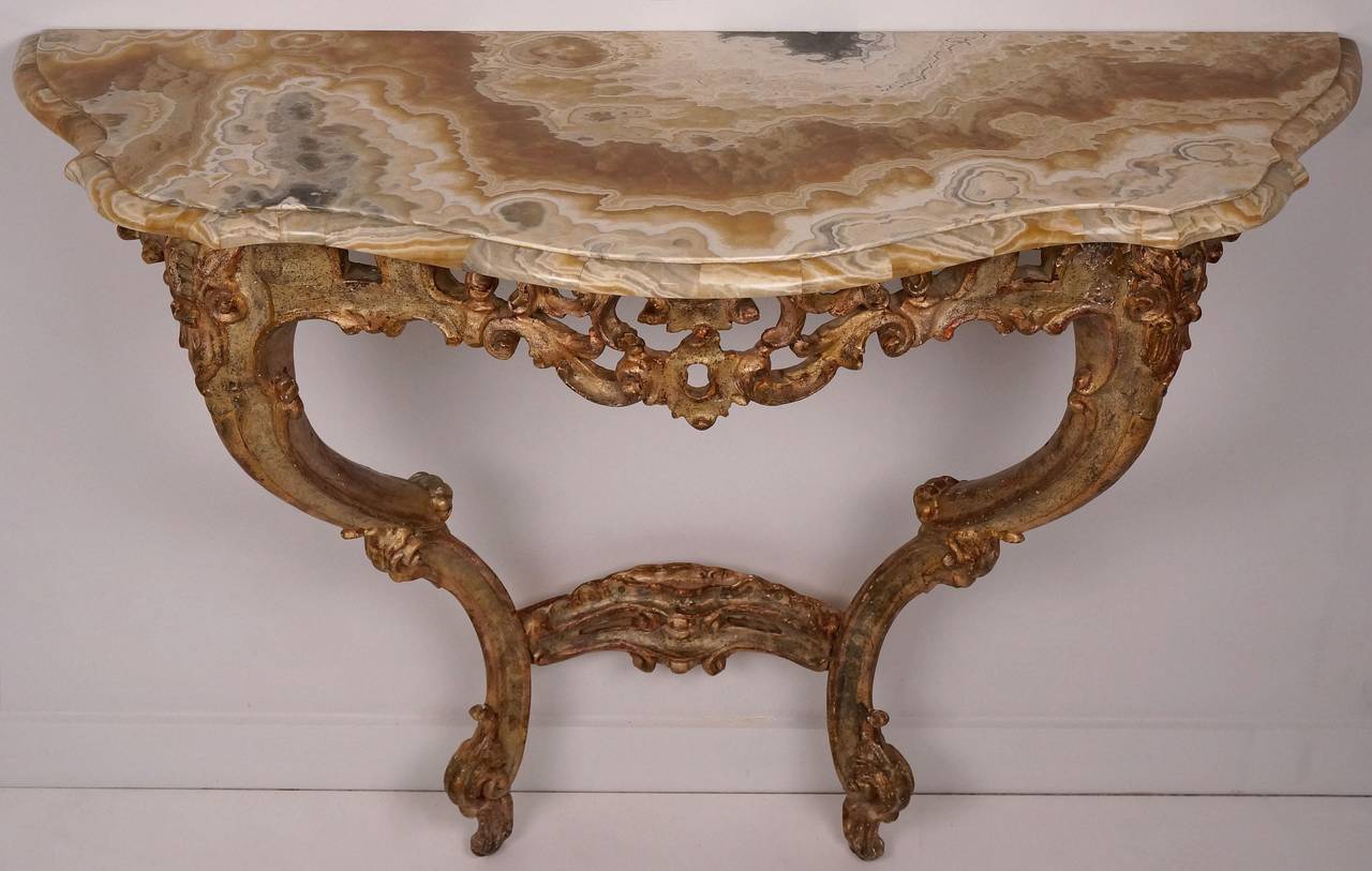 This beautiful Italian Rococo-Revival style giltwood wall mount console with an onyx top was created in the 19th century. With its serpentine top over a pierced rocaille carved apron raised on acanthus carved cabriole legs.
The finish is in a