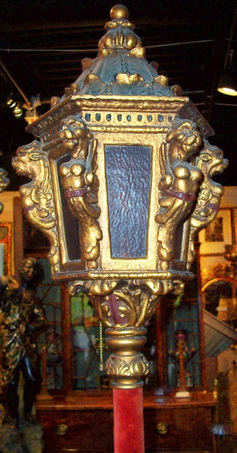 The typical design of a Venetian gondola lantern adapted to an interior pole lantern. The decorated base with pole (in red velvet) extending to a five pane (amber glass) lantern adorned with gargoyle type figures. The top with holes for heat vent.