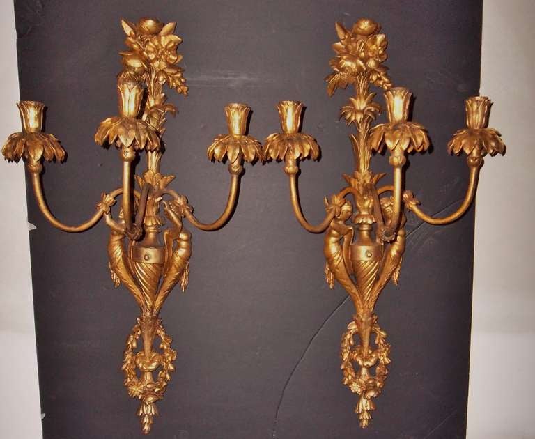 Pair of carved gilt sconces (drilled for electricity but currently not wired ). The central shaft of urn form with palm fond and top bouquet of flowers. The bottom with festoons and  garlands . The sides with caryatids.  Slender tole arms with palm