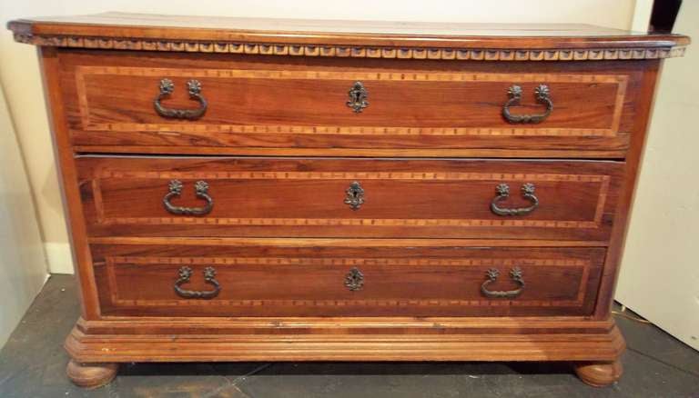 A Tuscan flavored chest of solid walnut  and iron hardware with boxwood inlay banding around each drawer. The top with dentil trim, the bottom with several layers of stepped bevel. All resting on stout bun feet .

Some fading  to the color.  A