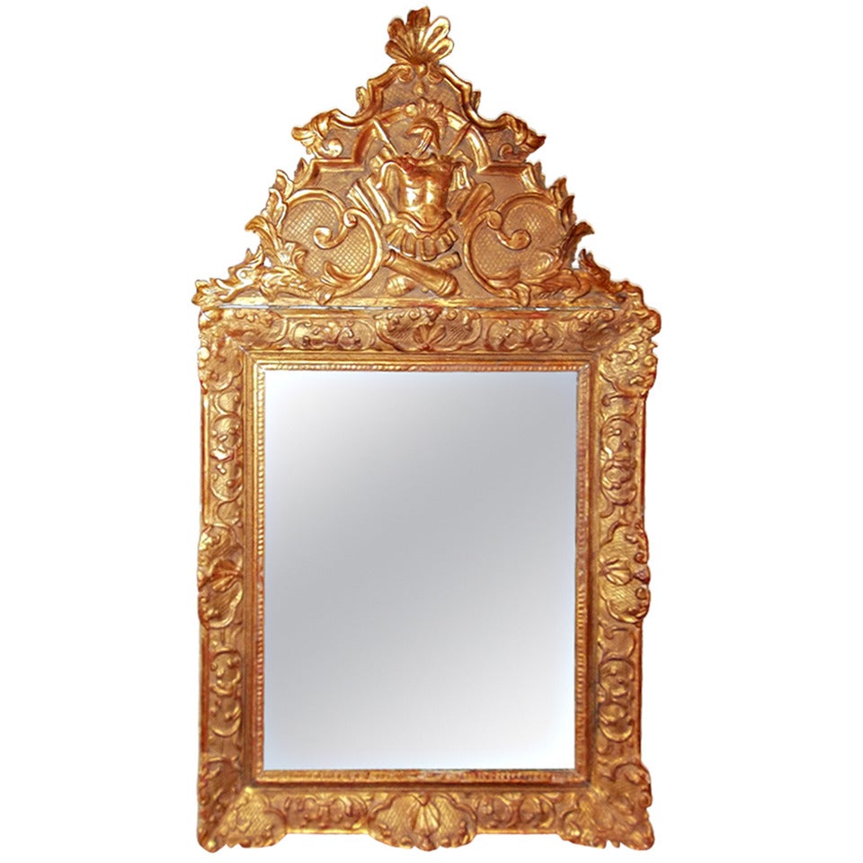 A carved, gessoed and gilded mirror frame with rocaille shells and 'c' scrolls 
surrounding a somewhat distressed plate. The frame crested with lower dragons 
flanking a very detailed and fine water gilt trophe' of armor and banners.

Wear to the
