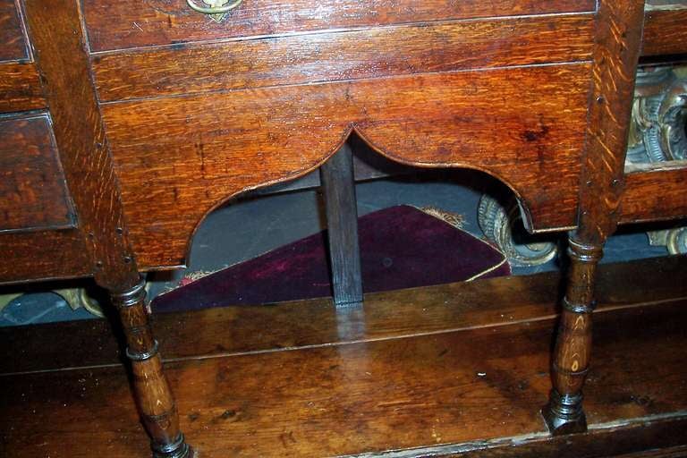Late 18th or early 19th century dresser base, sideboard or cupboard. Dark reddish oak with peg construction and original hardware. The pot board with fruitwood or similar surface supporting four front turned and shaped columns and three back