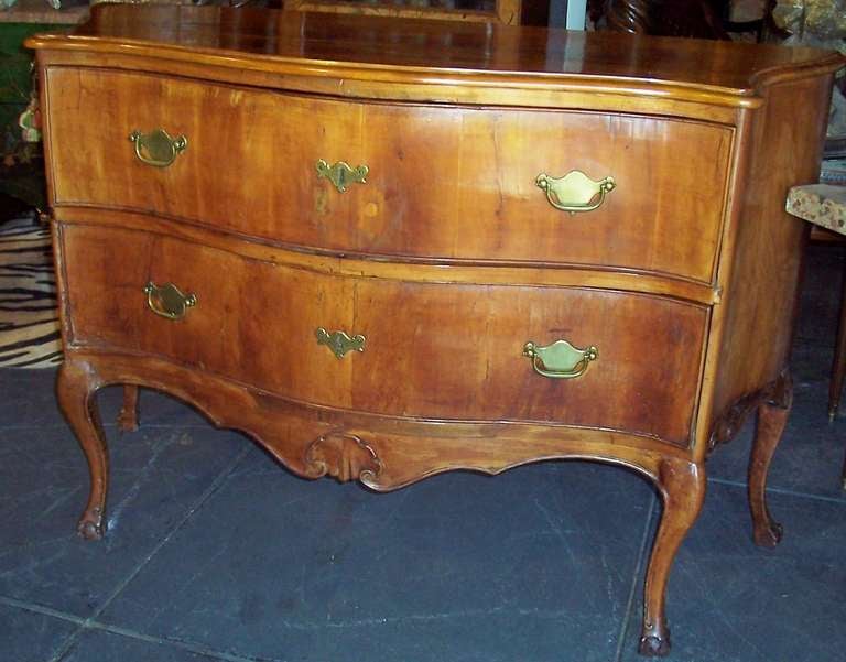 Fruitwood or a very faded walnut .
A classically simple cognac colored Italian commode with serpentine front / sides in late rococo taste. The bottom skirt on all three sides centered by a shell and then ending in claw and ball feet, Italian style.