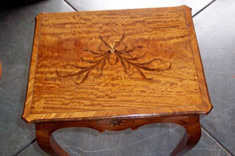 A table with tulipwood clad legs inlaid with satinwood panels on skirt flanking sunburst . The top with marvelous gold toned satinwood graining and faded color with tulipwood banding. The center with a ribboned laurel, each corner inlaid with