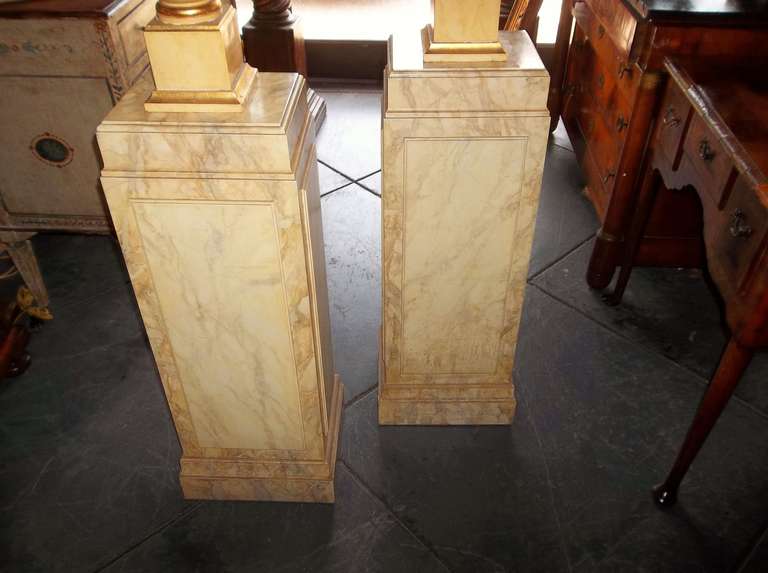 Pair of yellow painted and gilt highlighted neoclassical styled urns on later faux marble pedestals. The pedestals bottom weighted (so as not to tip over).

The urns in gloss yellow paint are probably France or Italy circa 1930's-1940's . The