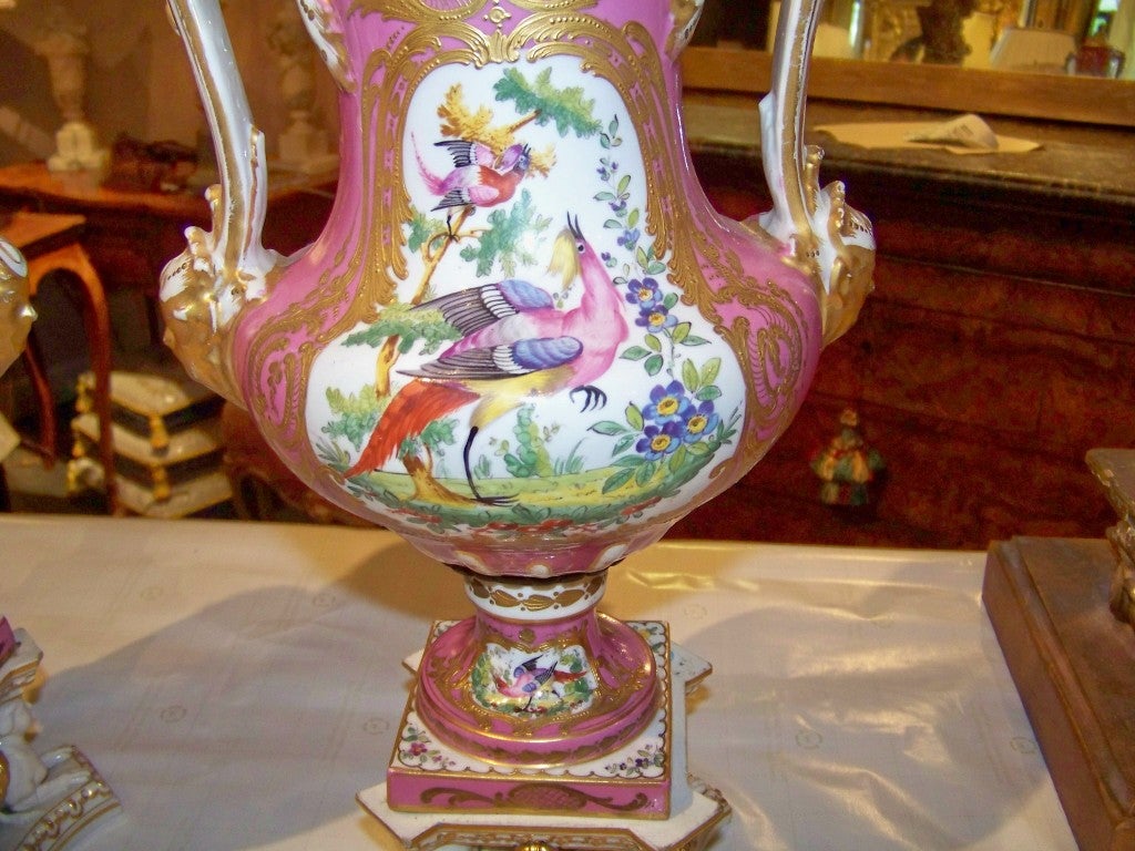 Pair of Chelsea style floral and fowl painted urns with later (20th century) Louis XVI style bases .Heavy honey gilding around the painted panels. Gold anchor mark on bottom (spurious?). Light rubbing to the gilt on the handles and on the bases.