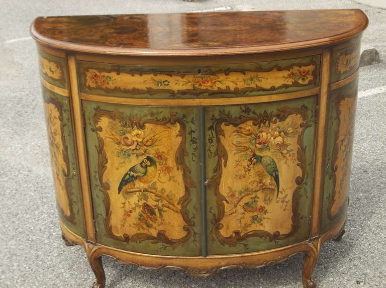 A lovely floral / fowl English (in the Italian taste) painted demilune commode , one drawer over a two door configuration (with two lesser doors flanking the central doors) . The colors, a very rich old world palette with exotic birds among floral