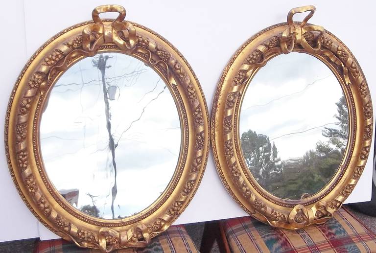 A pair of gilded (both in matte and highly burnished water gilt ) looking glasses , top and bottom with intertwining ribbons . Fruit and flowers are worked between the flow of the ribbon.

Both with a label for: Kimball, Whittemore & Co., on