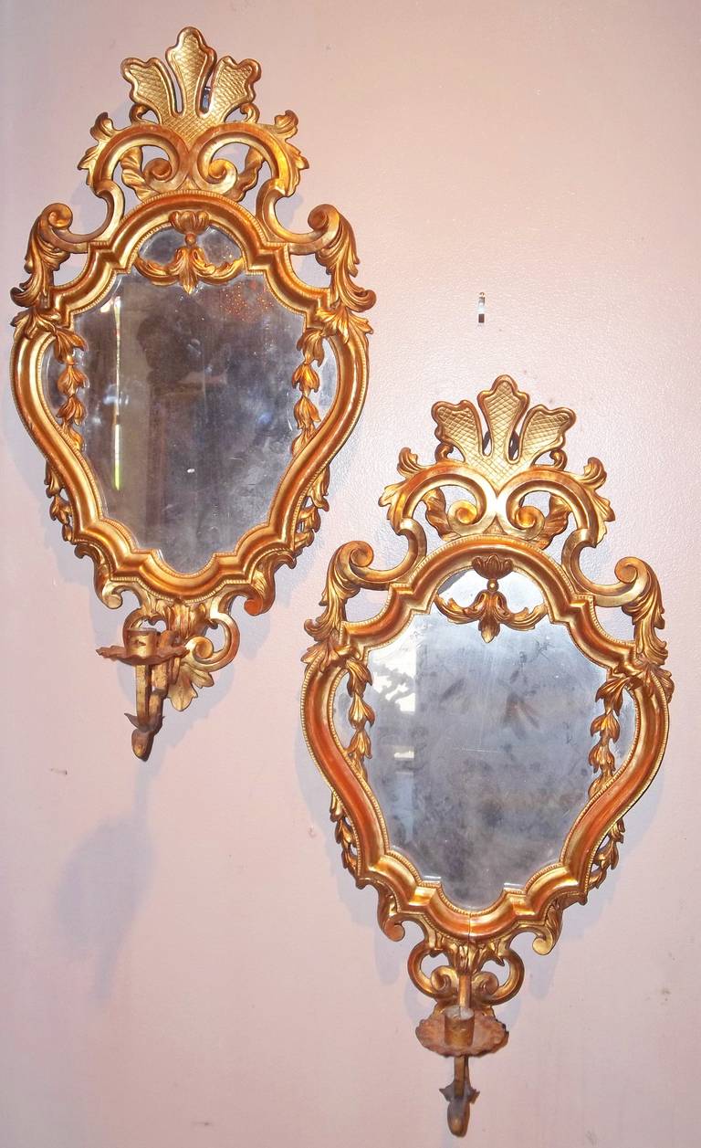 Carved wood frames, probably regilded (from the side appears to be a differing era of gilt ). Sconces are removable to make just mirrors. Lovely lemon gilt with red bole bleeding throughout. Water gilt.

Mirror plate spotty, losing some