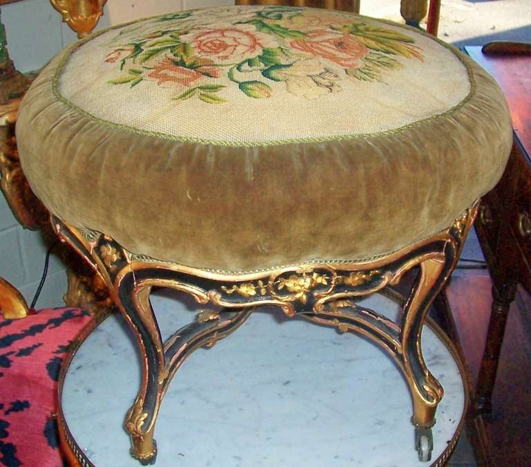 A floral carved stool or pouf with an overall terra cotta colored gesso. The black paint and red bole then applied and lastly the gold leaf . Significant chipping (as shown ) but rather charming blend of colors . The top with a tapestry type floral