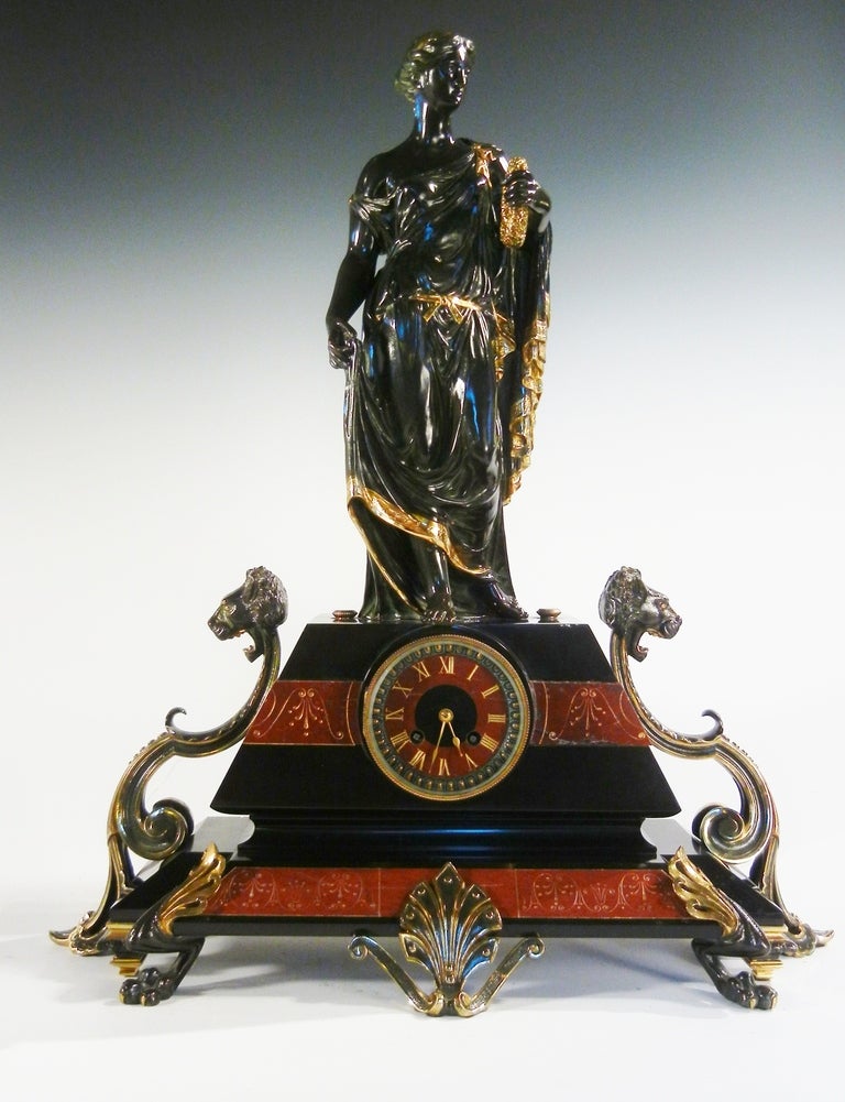 This symbolic clock from the Second French Empire is in bronze and marble and has the figure of Minerva holding a laurel wreath. The bronze figure has black and gilded patinas and stands on a black and red marble base containing the chiming clock,