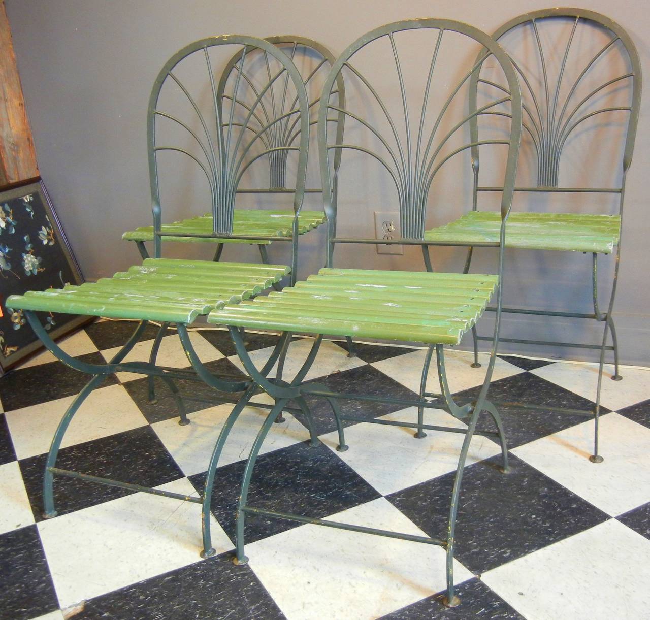 This set of four steel and wood garden or bistro chairs features folding wooden slats as seats, eight steel rods forming palm trees as backrests, and steel curule legs on penny feet. The chairs are in their original green-painted finish and old