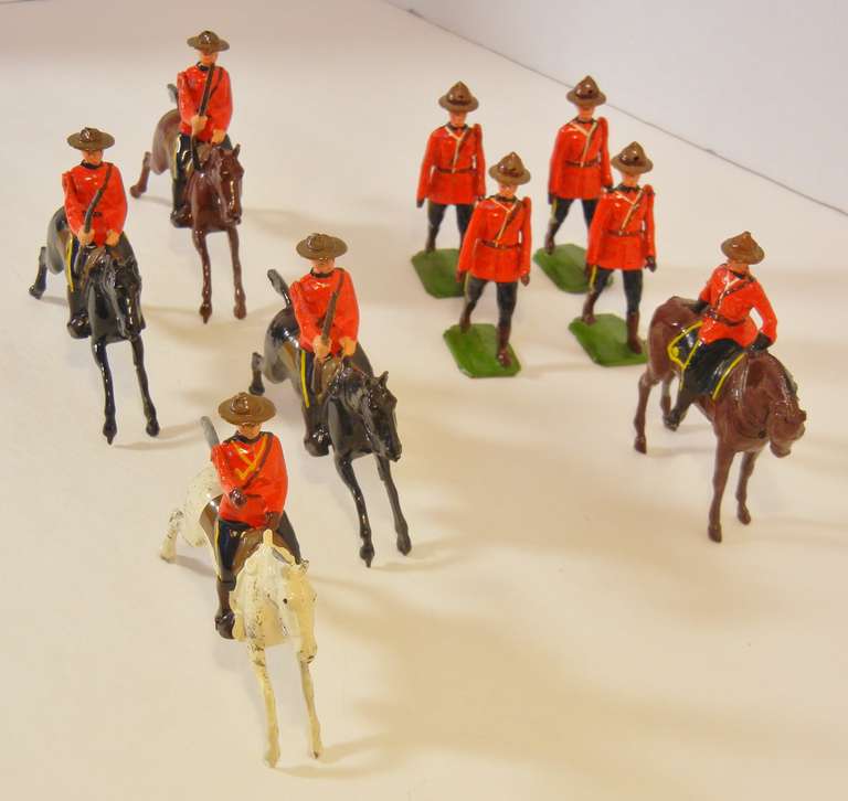 This grouping of nine hand-painted lead alloy toy soldiers by William Britains, Ltd., consists of two sets made in London circa 1960-1966. They all wear red tunics and brown Mountie hats.

Set #1349 (four pieces):  