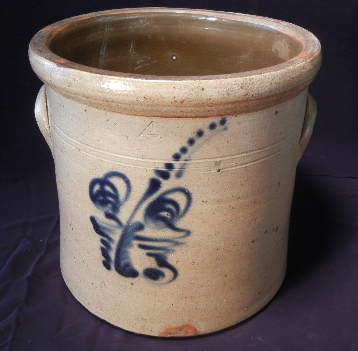 Hand-thrown, salt-glazed, four-gallon stoneware crock with a cobalt blue under-glaze, hand-painted, stylized cinnamon fern. There is a band of  double incised lines around the neck connecting the two ear-shaped handles. The top rim is molded and