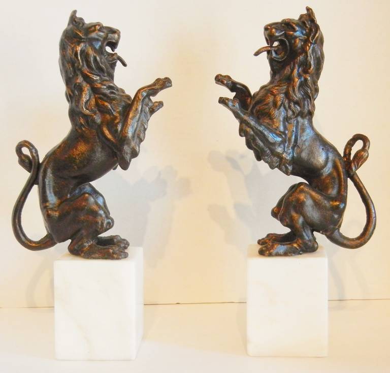 This pair of bookends feature heraldic rampant lions on square white marble plinth bases. They are solid cast iron with a bronze wash. Since they weigh nine pounds each, they are practical and useful and are able to secure large sets of books, as