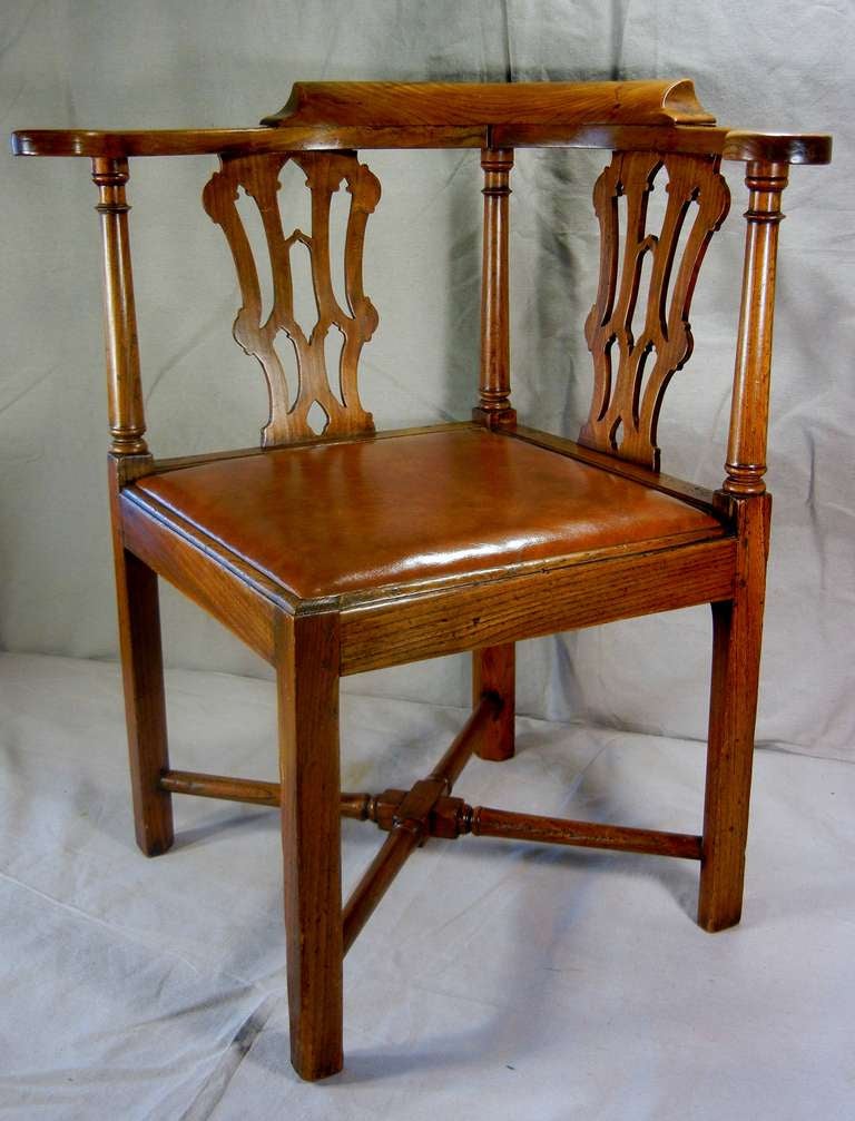 This country Chippendale corner chair is made of elm and has a reupholstered saddle leather drop-in seat. It is in the Chippendale Gothic style, with a pillow-shaped crest rail, out-curving arms with hand-holds, two scrolling cut-out back spats,