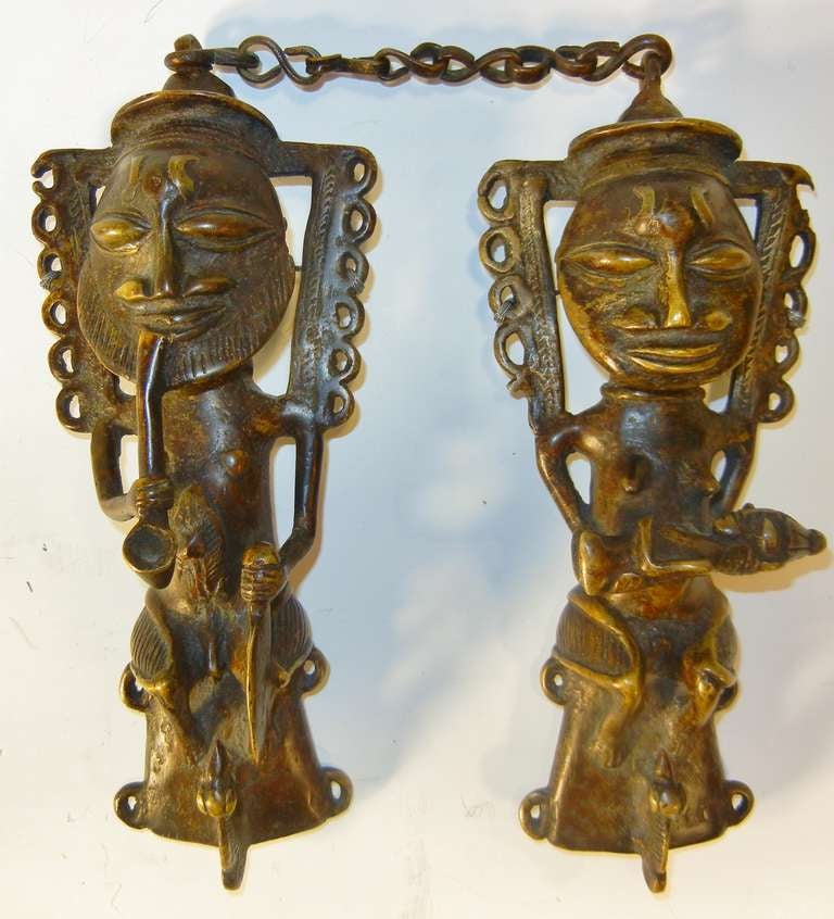 This pair of Edan figures, a male smoking a pipe and a female holding an infant, are attached at the heads by a chain. They are made of sand-cast bronze and have a fine, natural patina. They are major symbolic objects of power among the Yoruba