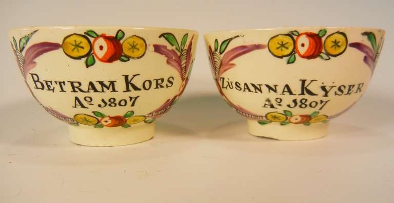 This pair of Staffordshire lead-glazed creamware teabowls are hand-painted in enamel colors with swags of roses, cherries, cornucopias, oranges and apples around the names of Betram Kors and Zusanna Kyser, and they are dated 1807. They commemorate