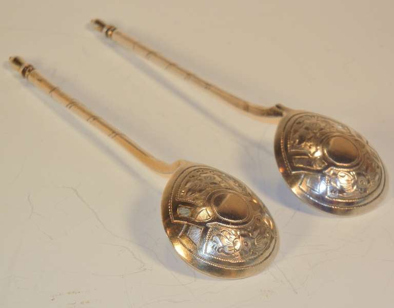 This pair of Russian silver teaspoons have plain ovoid bowls, the back of which are hand-engraved with traditional Russian floral and leaf designs inside panels around a central circle; the shafts are engraved with spiraling double lines which end