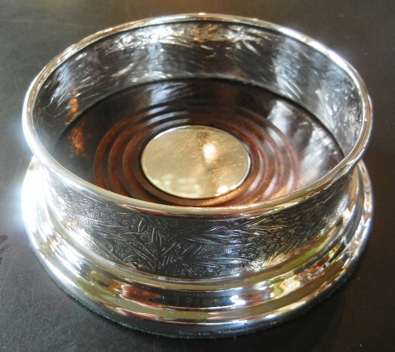 Sterling silver Audubon pattern wine coaster by Tiffany & Co., c. 1950, embossed with repousse and chased work depicting birds, foliage and flowers and a spider web. The interior base of the wine coaster is mahogany centered with a sterling silver