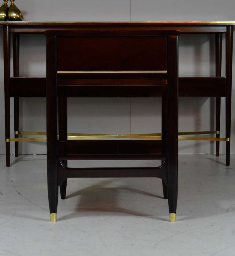 A pair of newly refinished mid century tiered side tables featuring brass trim along single drawer handle and feet.