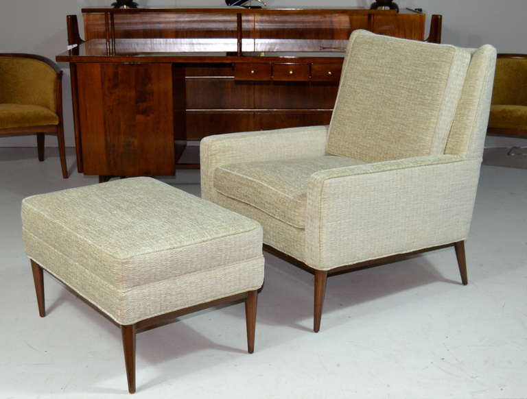 Handsome lounge chair and ottoman newly upholstered in a very subtle beige chenille, base newly refinished in medium walnut by Paul McCobb for Directional.