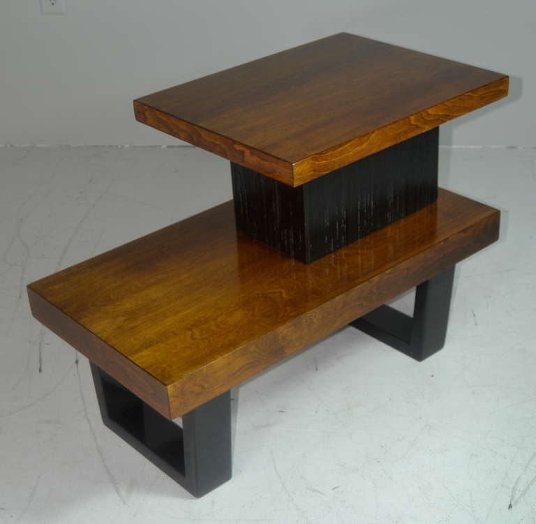 A pair of tiered two-tone side tables designed by Paul Frankl. Legs and combed oak center structured have been refinished in ebony, emphasizing the beautiful natural walnut tops.