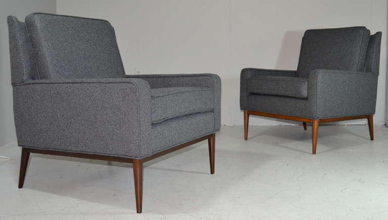 A pair of Mid-Century modern classic lounge chairs designed by Paul McCobb for Directional. Chairs have been newly upholstered in a very masculine smokey grey felt with all new foam and insides. Walnut bases newly refinished in natural.