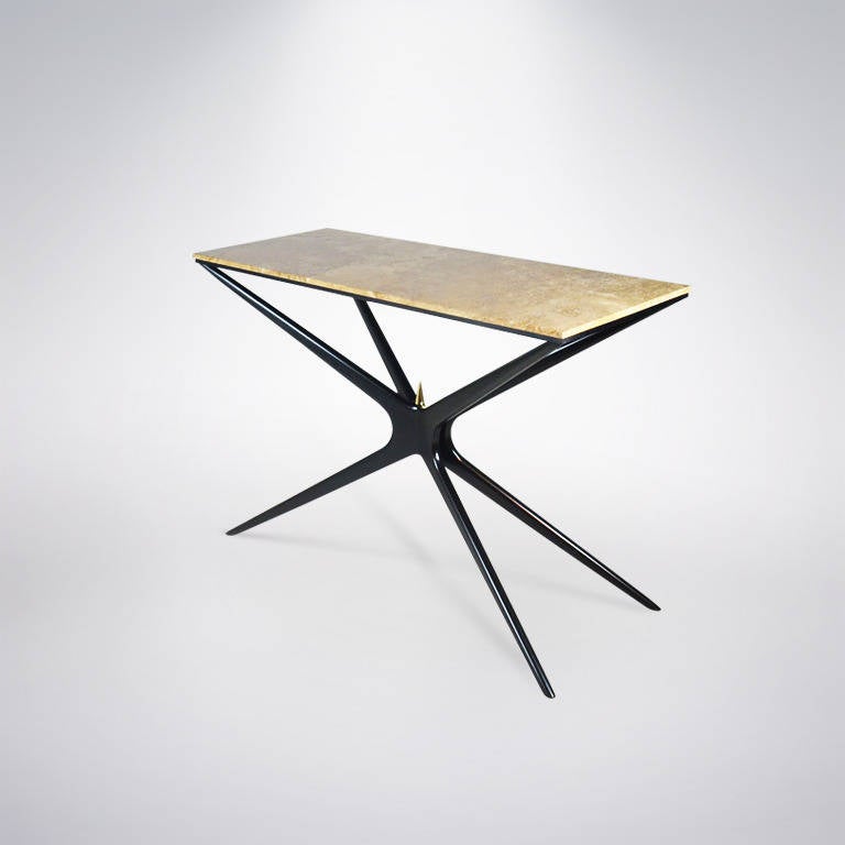 
The Gazelle console table is a slender piece shown here in an ebony finish with a marble top. Tapered legs and arms that converge in the center making an X-shaped base; on top of the X is the signature brass spear tip. The legs are handcrafted,