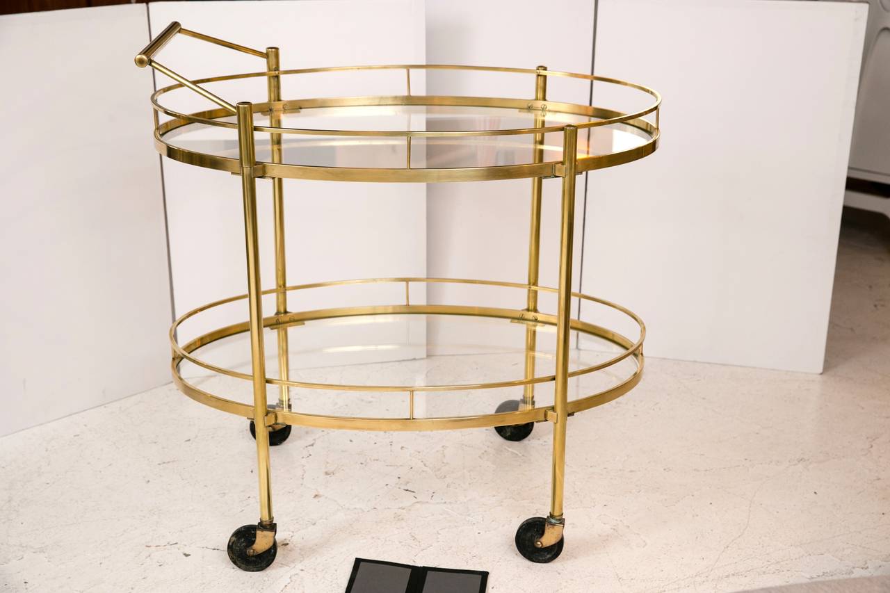 Classic 1960s oval solid brass bar cart with beautiful proportions and in all original condition. Very well made, functional and lovely. There is a very slight chip in one piece of the oval glass, which does not detract in any way from this