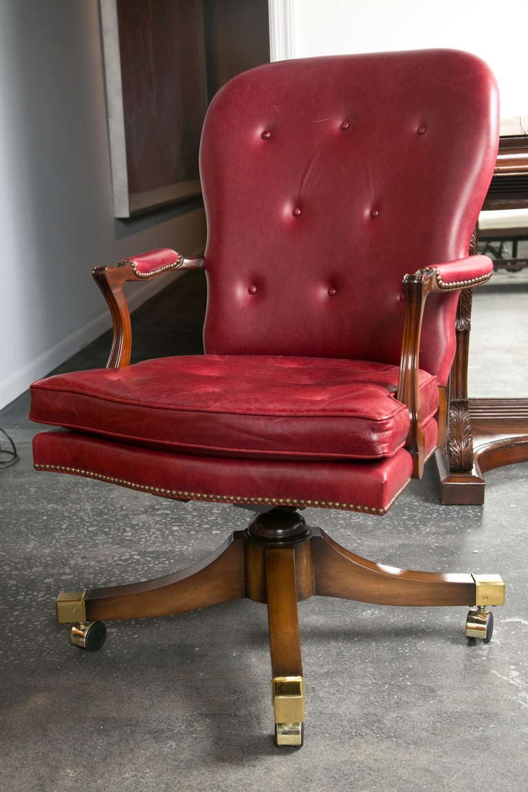 A classic, British style castored red leather chair of a very fine quality. Wood pedestal base has brass end-caps and the arms and seat have brass nail-head trim. Great condition button-tufted red leather upholstery.