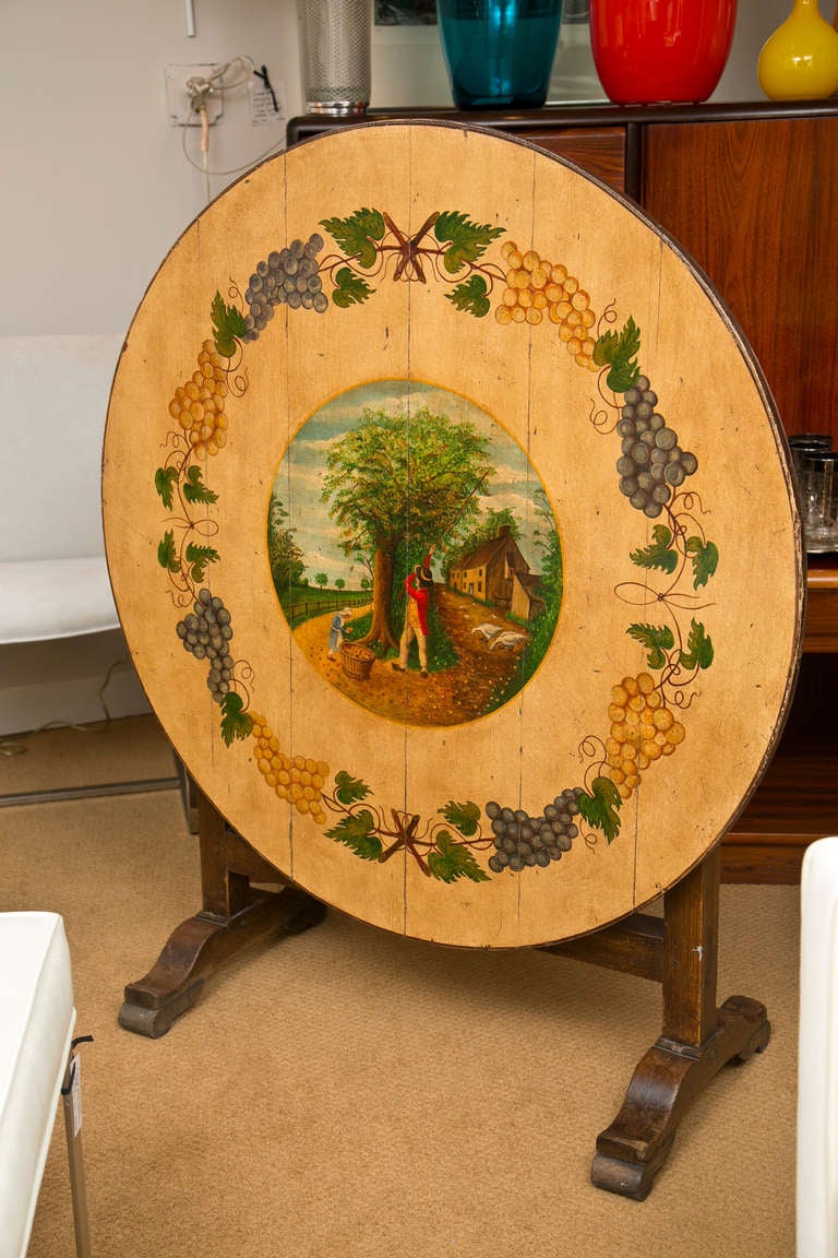 Mid 19th Century solid oak wine table in excellent condition. Top surface has is hand painted with a creme background against which a primitive orchard gathering scene is bordered by grape leaves and foliage.