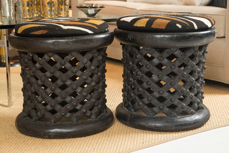 A fine, compatible pair of West African single trunk carved ottoman or footstools that have a custom upholstered seat cushion. The trunks are hand-carved in traditional tribal style, and the cushions are covered in authentic handwoven African