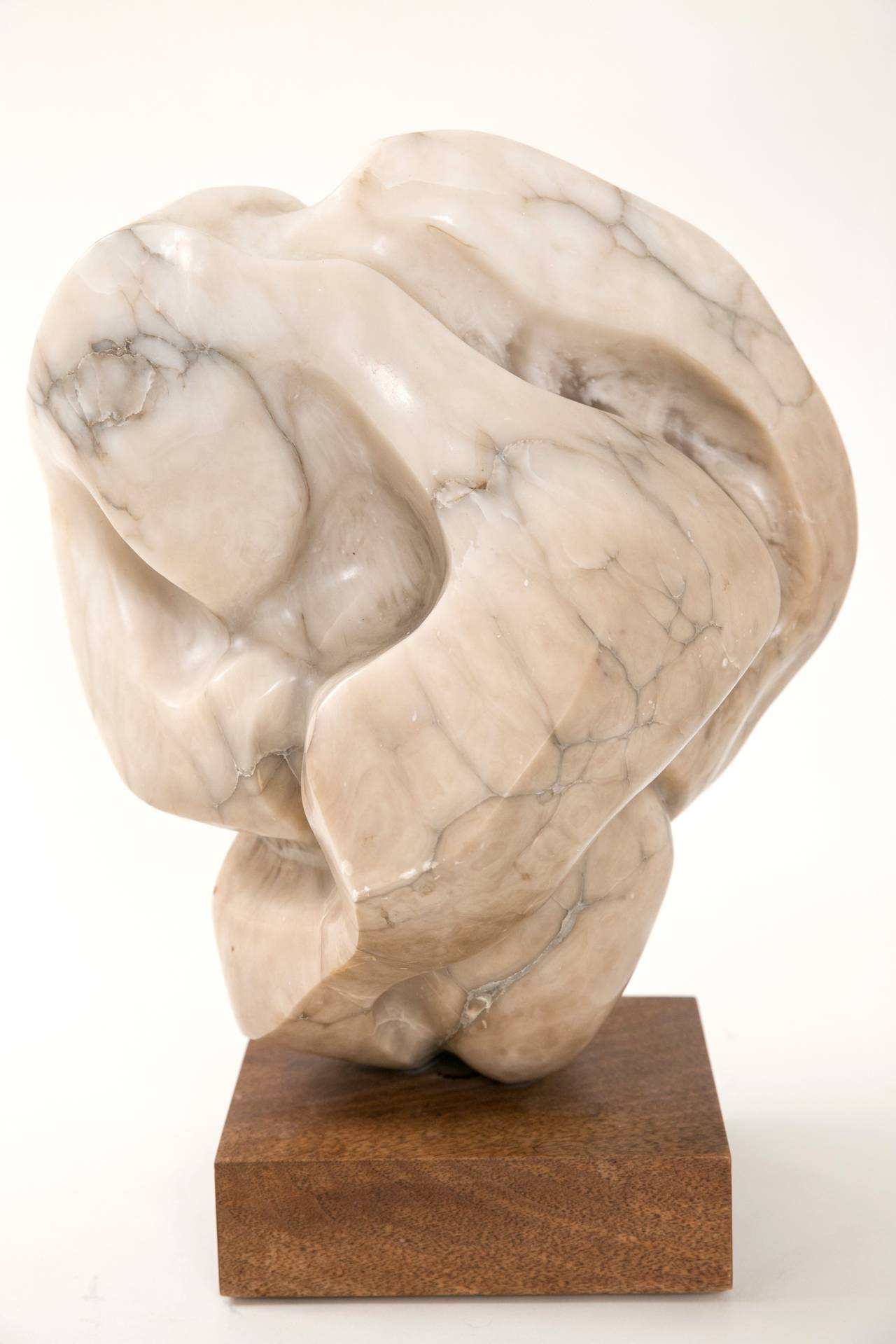 Carved in New York in the 1960s, this veined alabaster sculpture is in excellent condition. Unsigned, the piece shows influences as wide ranging as Barbara Hepworth, Isamu Noguchi, and Eskimo stone work! Custom wood Stand.