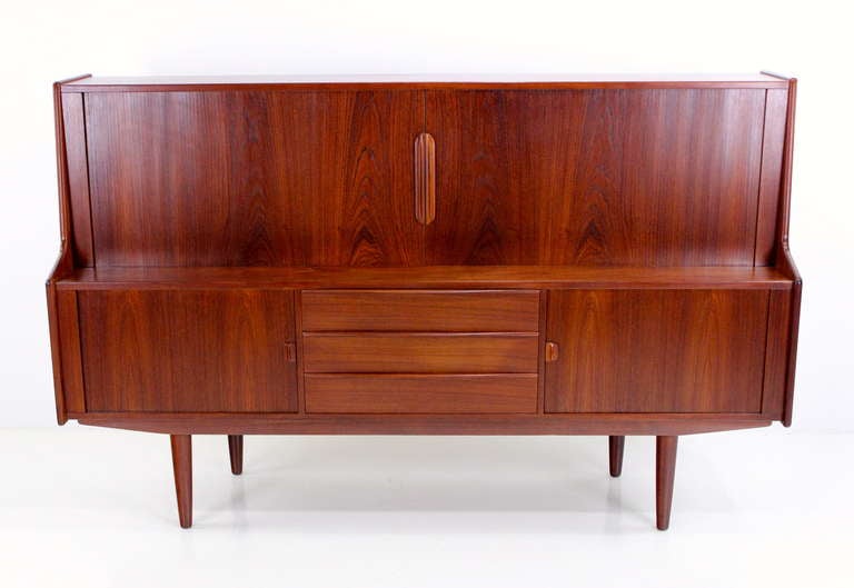 Danish modern credenza designed by Kofod Larsen.
Teak with rich, consistent grain.
Tambour doors in upper portion glide open to adjustable shelving and four removable felt lined drawers.
Lower portion features sliding doors opening to adjustable