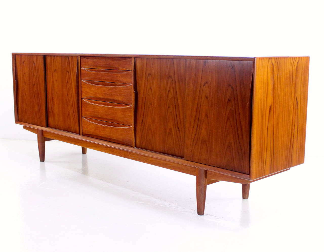 Danish modern credenza by Dyrlund.
Richly grained teak with classic lines and beautifully sculptured handles.
Five drawers in the center, the top two are felt lined.
Sliding doors open to adjustable shelves on each end.
Finished on the back for