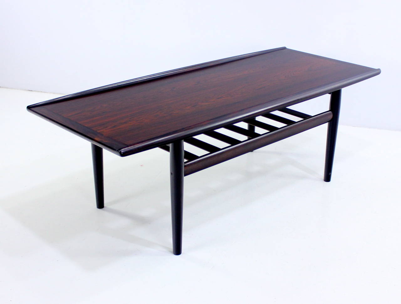 Extraordinary Danish modern coffee table designed by Grete Jalk.
Richly grained rosewood.
Table top has solid, sculptured, upturned edges.
Beautifully slated lower magazine shelf.
Professionally restored and refinished by LookModern.
Matchless