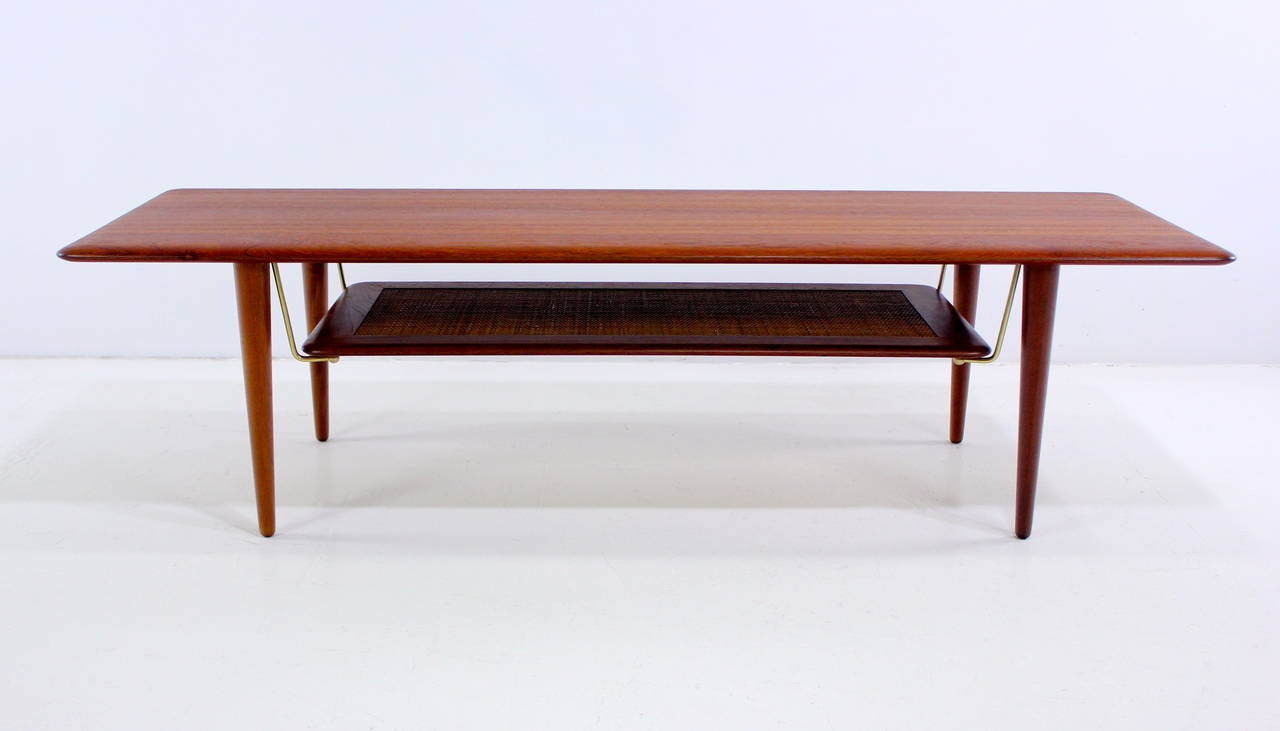 Danish modern cocktail or coffee table designed by Peter Hvidt.
France & Son, maker.
Richly grained solid teak. Lower caned magazine shelf with brass accents. 
Round version and side tables also available.
Designed to compliment Hvidt's