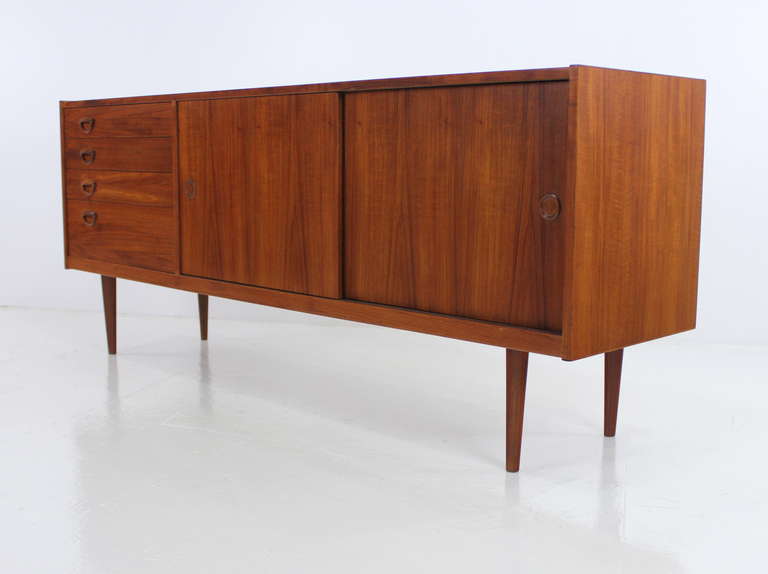 Danish modern credenza designed by Kai Kristiansen.
Richly grained teak.
Sliding doors open to adjustable shelving in center and right.
Four drawers on left.
Signature circular Kristiansen handles and pulls throughout.
Professionally restored