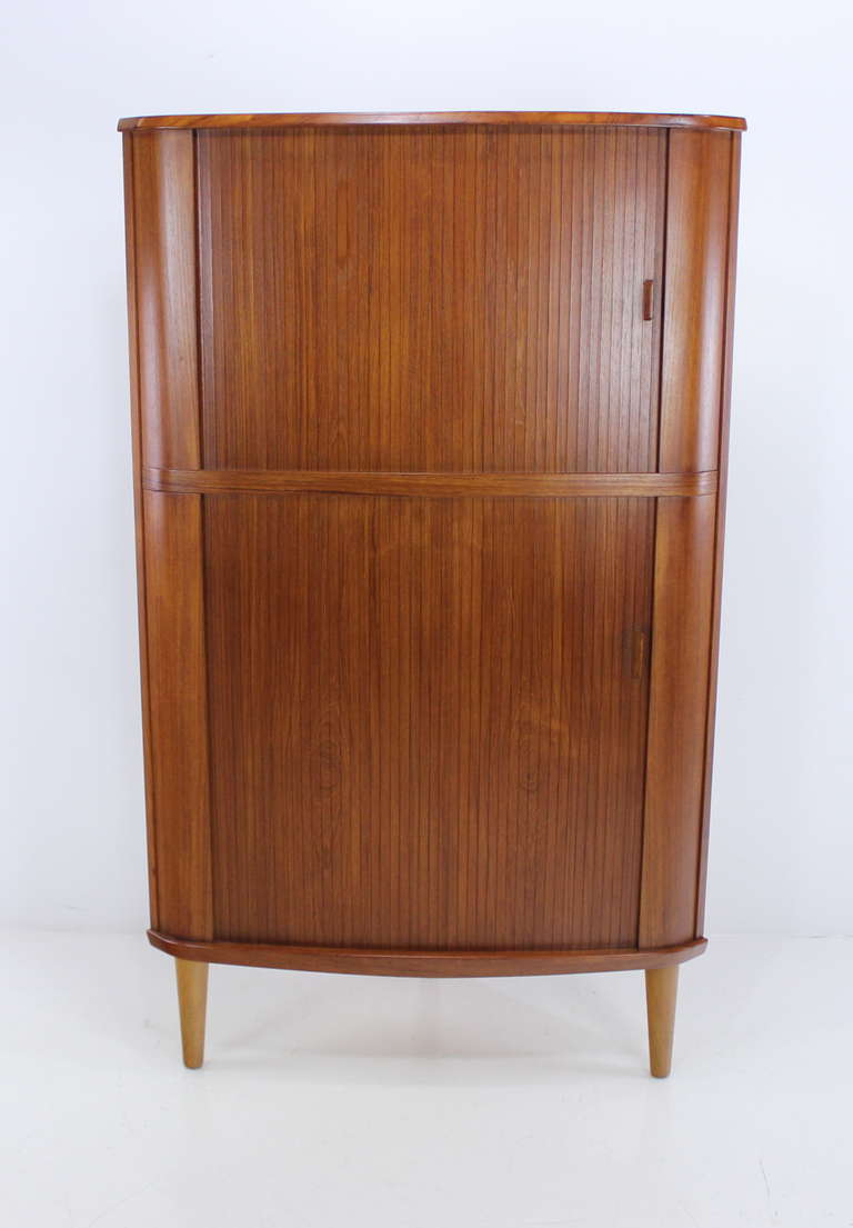 Danish modern corner cabinet designed by Skovmand Andersen.
Rich teak with birch interior.
Tambour doors open to adjustable shelves throughout.
Top two shelves are felt-lined.
Professionally restored and refinished by LookModern. 
Matchless