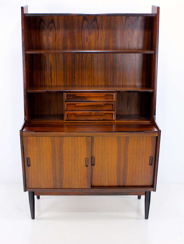 Danish modern secretary.
Richly grained rosewood.
Pull out writing surface. Bookshelf top with three drawers.
Sliding doors on bottom open to adjustable shelving.
Professionally restored and refinished by LookModern.  
Matchless quality and