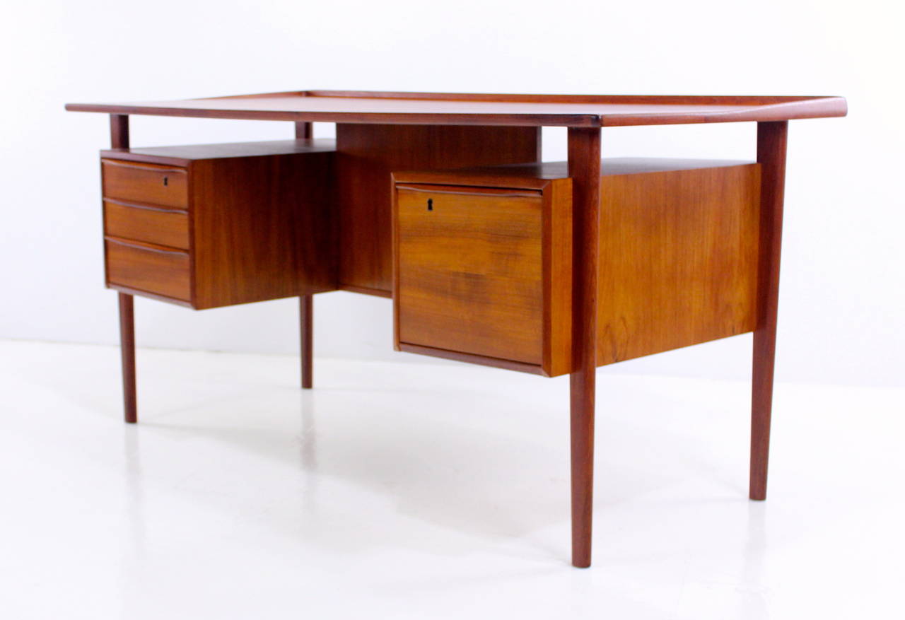 Danish modern desk designed with executive swag by Peter Løvig Nielsen in 1974.
Richly grained teak.
Floating top with sculptural lip rising from sides to back edge.
Locking file drawer on right, three drawers on left, the top drawer
