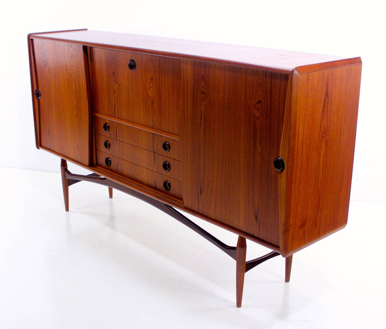 Danish modern credenza with impressive style and size.
Richly grained teak with hardwood edging.
Beautifully crafted base supports extraordinary cabinet.
Sliding doors on each end open to adjustable shelves.
Drop down door opens to lighted