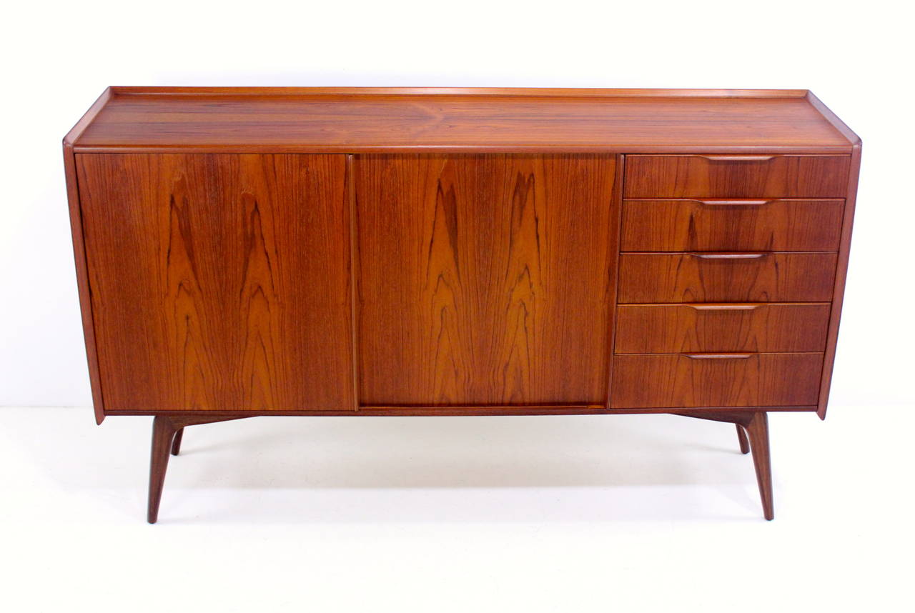 Danish modern sideboard / credenza designed by Harry Ostergaard.
Early piece manufactured by A.S. Randers Møbelfabrik.
Rich teak with spectacular top graining.
Sliding doors open to adjustable shelves in left and center.
Five drawers with