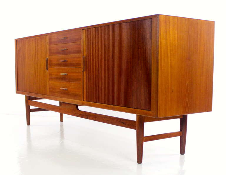 Danish modern credenza designed by Erik Worts.
Richly grained teak with birch interior throughout.
Tambour doors open to adjustable shelves on left and five pull out trays on the right.
Five drawers in the middle.
Hand carved handles with